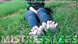 Goddess displays cute curly toes in white socks beneath jeans on spring grass field