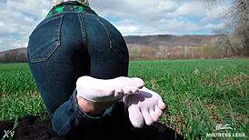 Goddess displays cute curly toes in white socks beneath jeans on spring grass field
